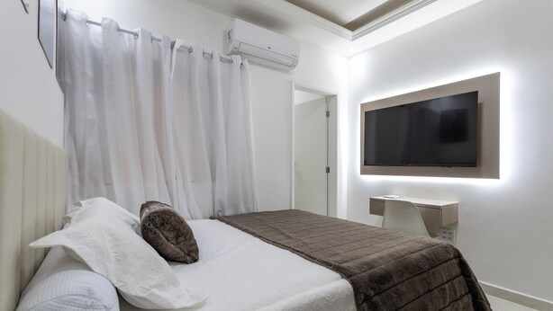 Un dormitorio con cama, televisor de pantalla plana montado en la pared, mesita de noche y aire acondicionado.