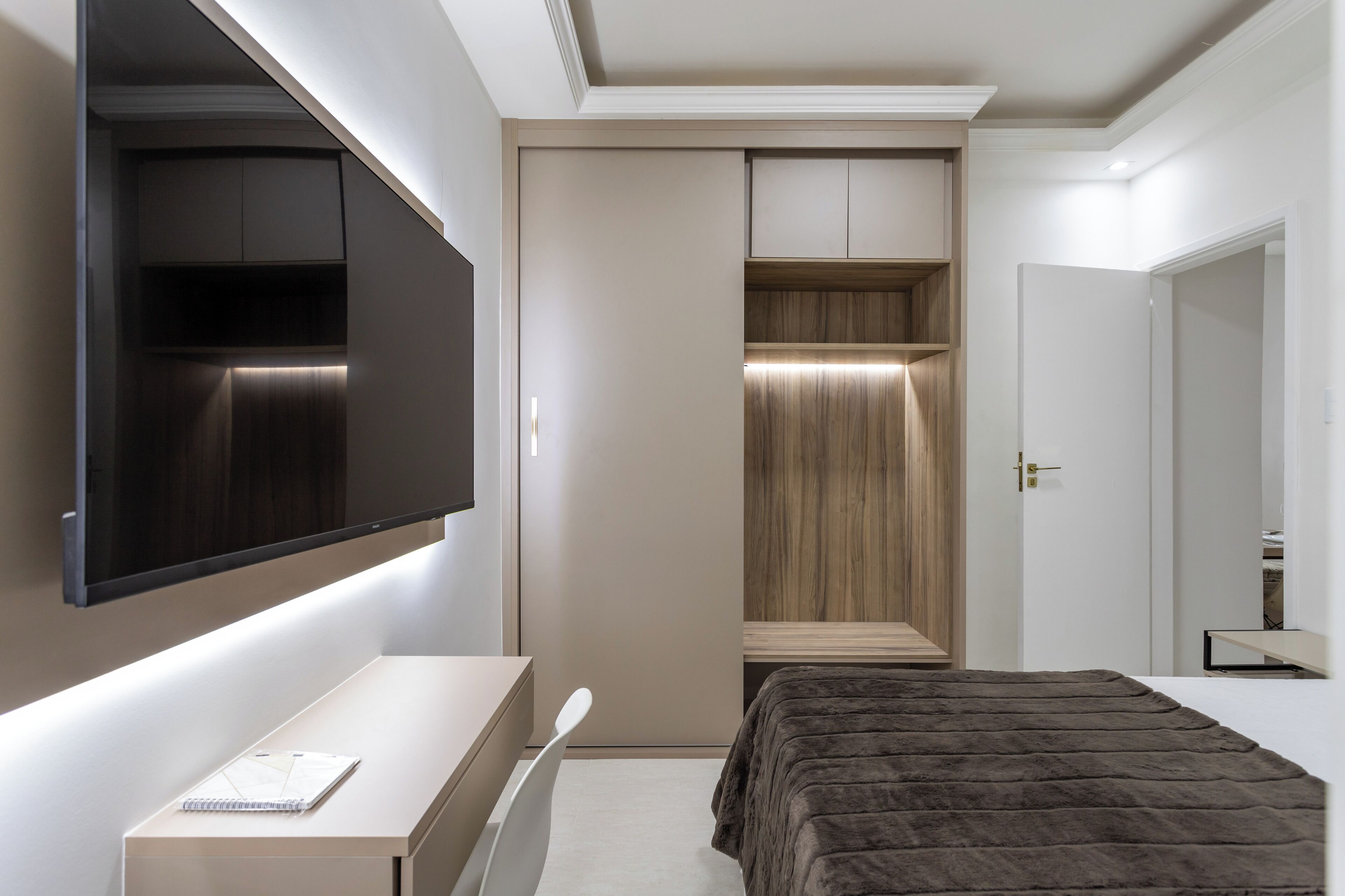 Een slaapkamer met een bed, een bureau, een kledingkast en een aan de muur bevestigde televisie.