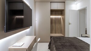 Un dormitorio con cama, escritorio, armario y televisor montado en la pared.