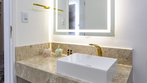 Un baño moderno con lavamanos blanco, encimera de mármol y un espejo grande con iluminación integrada.