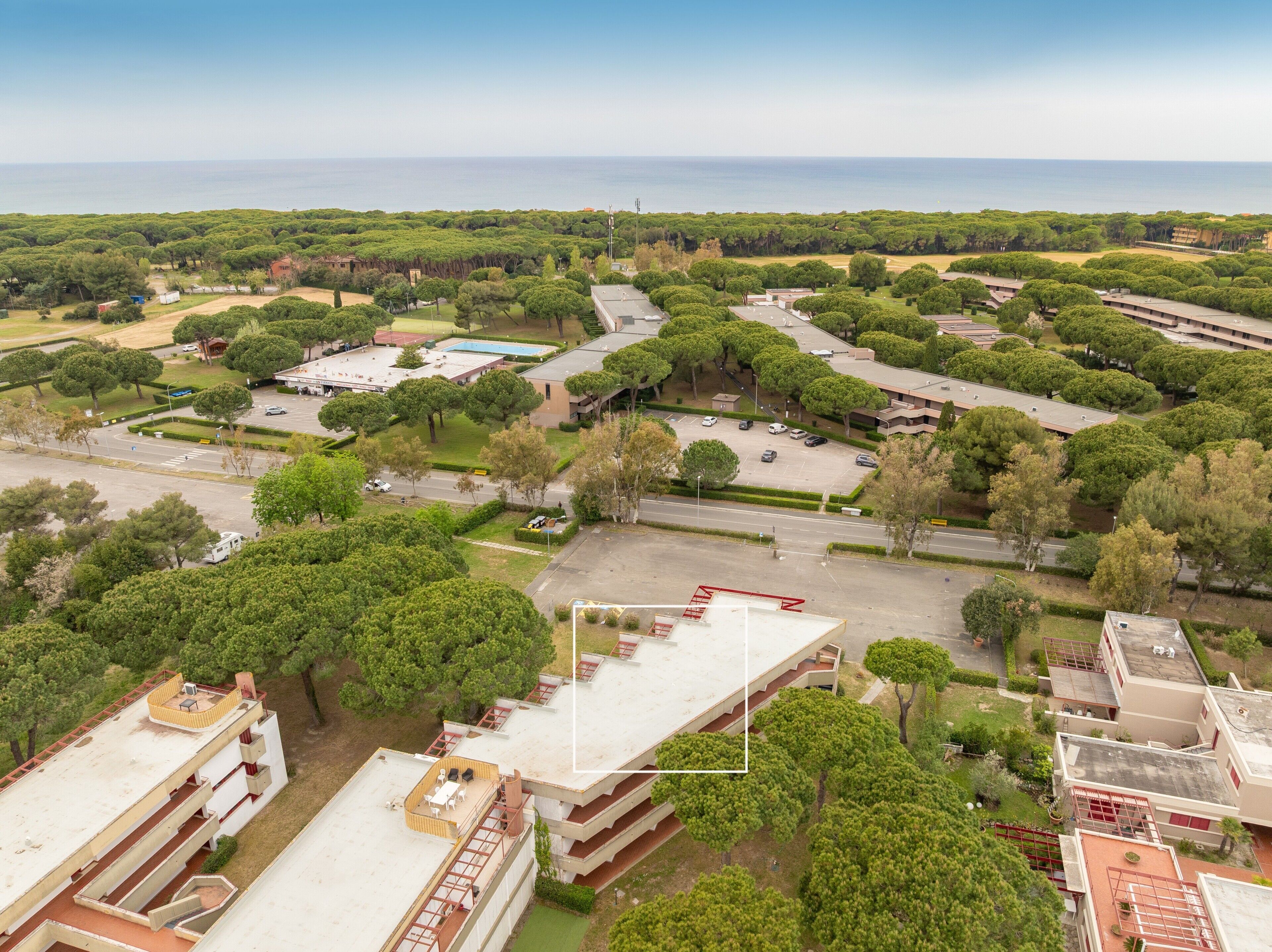 An aerial view of a residential area with multiple buildings, green spaces, and a clear view of the sea.