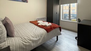 A bedroom with a bed, a window with a view, a painting on the wall, and a wardrobe. - Downtown Sheffield Retreat (Sheffield)