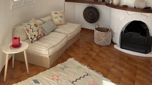 A cozy living room with a sofa, a fireplace, a hanging lamp, and a colorful painting. - Minorcan house (S'Algar)
