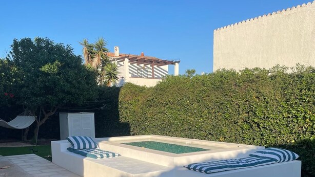 A modern outdoor seating area with a pool, surrounded by a well-maintained lawn and a hedge. - Minorcan house (S'Algar)
