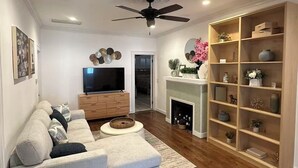 Een woonkamer met een bank, televisie, open haard en houten planken.