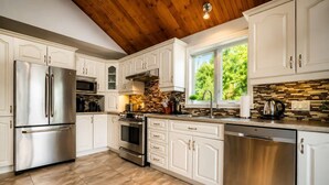 Une cuisine moderne dotée d’appareils électroménagers en acier inoxydable, de meubles blancs, d’un pare-feu en pierre et d’un plafond en bois.