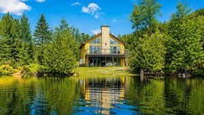 Une maison dotée d’un grand balcon, entourée d’arbres et bordée par un lac.
