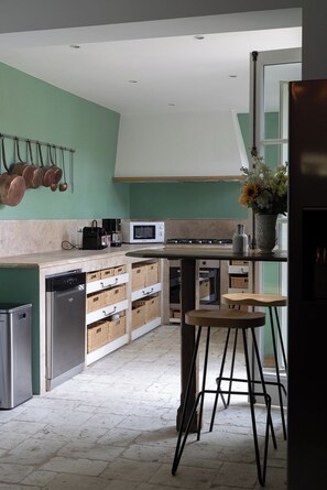 Una cocina moderna con lavavajillas, microondas y estufa, una barra con taburetes y un colgador para ollas.