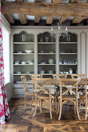 Un comedor con mesa y sillas de madera, un armario empotrado con estantes llenos de vajilla y una lámpara de araña.