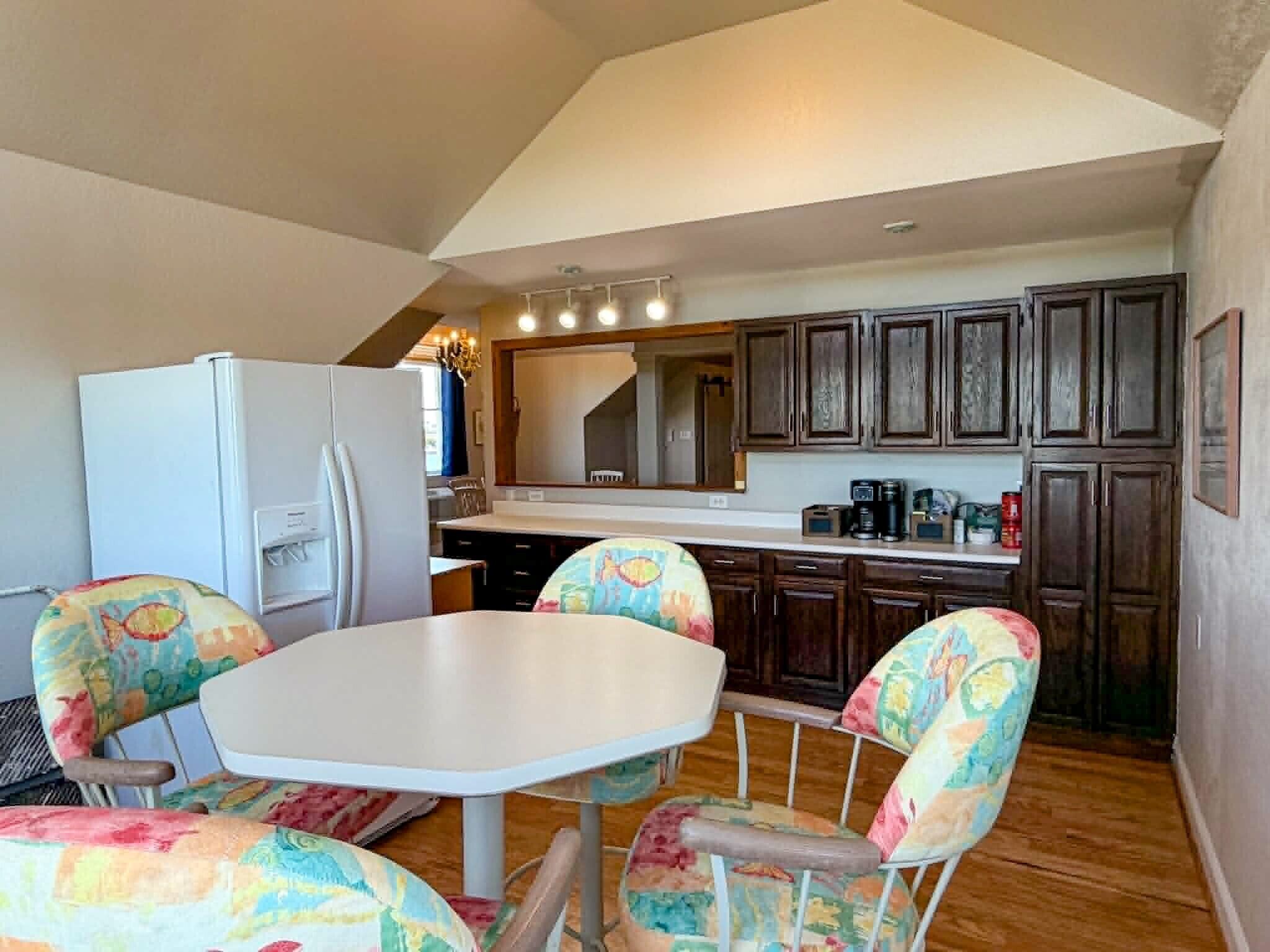 A kitchen with a dining table and chairs, wooden cabinets, a refrigerator, and a chandelier.