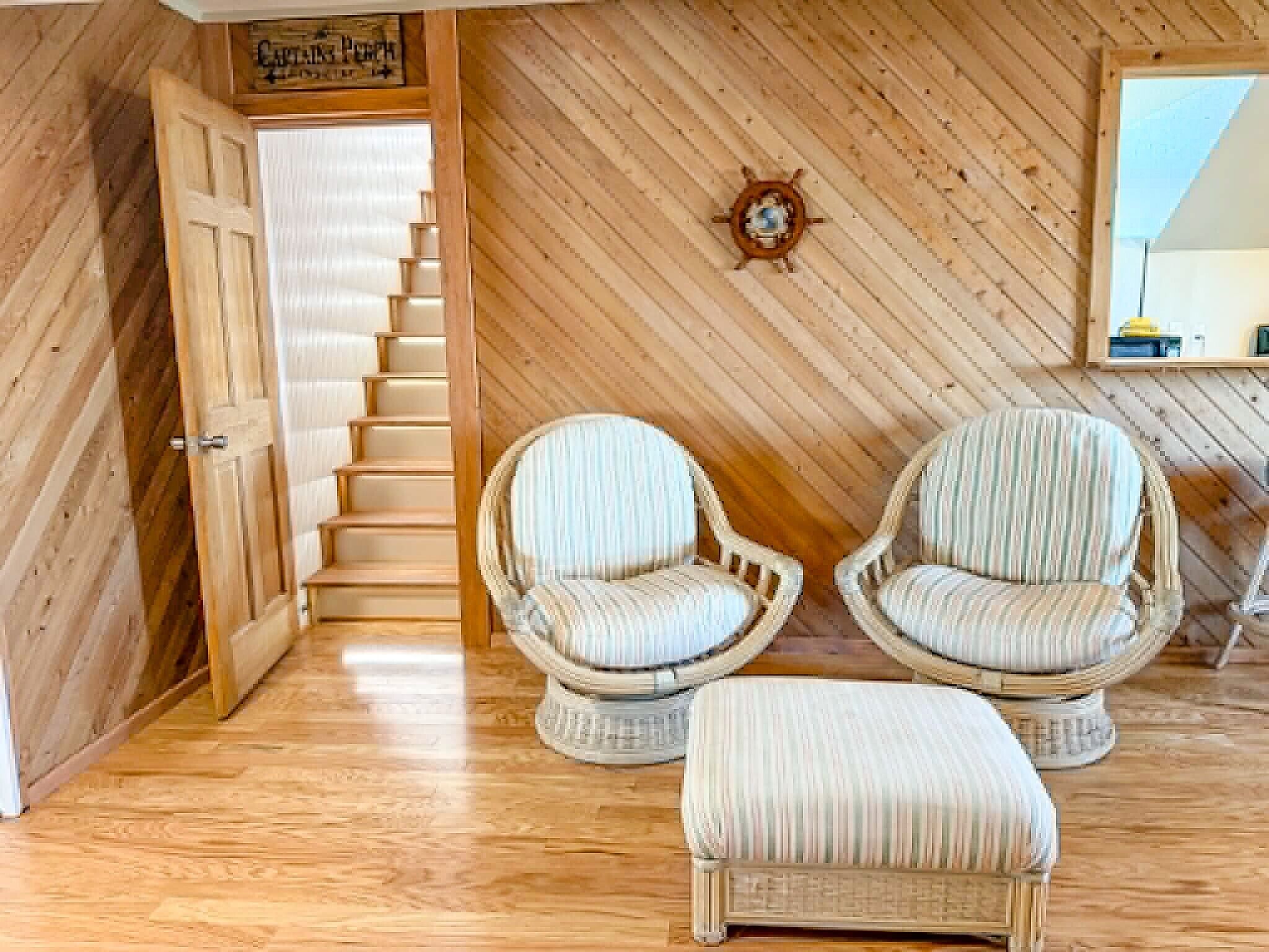 Un interior de madera con una escalera, dos sillones de mimbre, un reposapiés acolchado y un espejo colgado en la pared.
