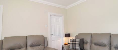 A room with two beige leather sofas, a white door, a lamp, and a ceiling light fixture.