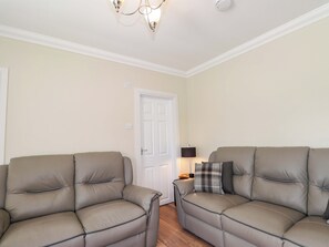 A room with two beige leather sofas, a white door, a lamp, and a ceiling light fixture. - Craig Cottage (Banff)