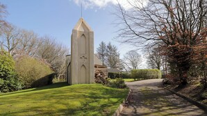 En kirke med et spidst tårn, en belagt indkørsel og velplejede græsplæner.