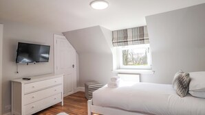 Et soveværelse med en seng, et tv ophængt på væggen, en kommode og et vindue med udsigt.