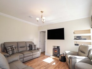 A living room with a sofa, a fireplace, a television, and a ceiling light fixture. - Craig Cottage (Banff)