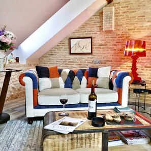A cozy living room with a brick wall, a sofa with colorful cushions, a wine bottle, and a magazine on a coffee table. - Hostcare - Stella Matutina · lift (Sarlat-la-Canéda)
