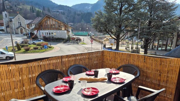 Una terrazza con un tavolo apparecchiato per mangiare, affacciata su una città con una chiesa e una montagna sullo sfondo.