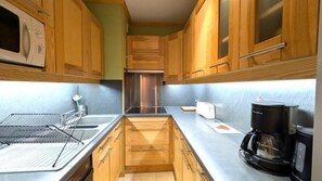 Una cocina compacta con armarios de madera, un lavamanos de acero inoxidable, un tostador y una cafetera.