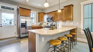 A kitchen with wooden cabinets, a stainless steel refrigerator, a microwave, and a large island with bar stools. - Riverwalk Path! Heart of South Main w/ Peak Views (Buena Vista)