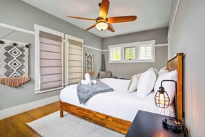 Ein Schlafzimmer mit Bett, Deckenventilator, Nachttischlampe und einem Fenster mit Jalousien.