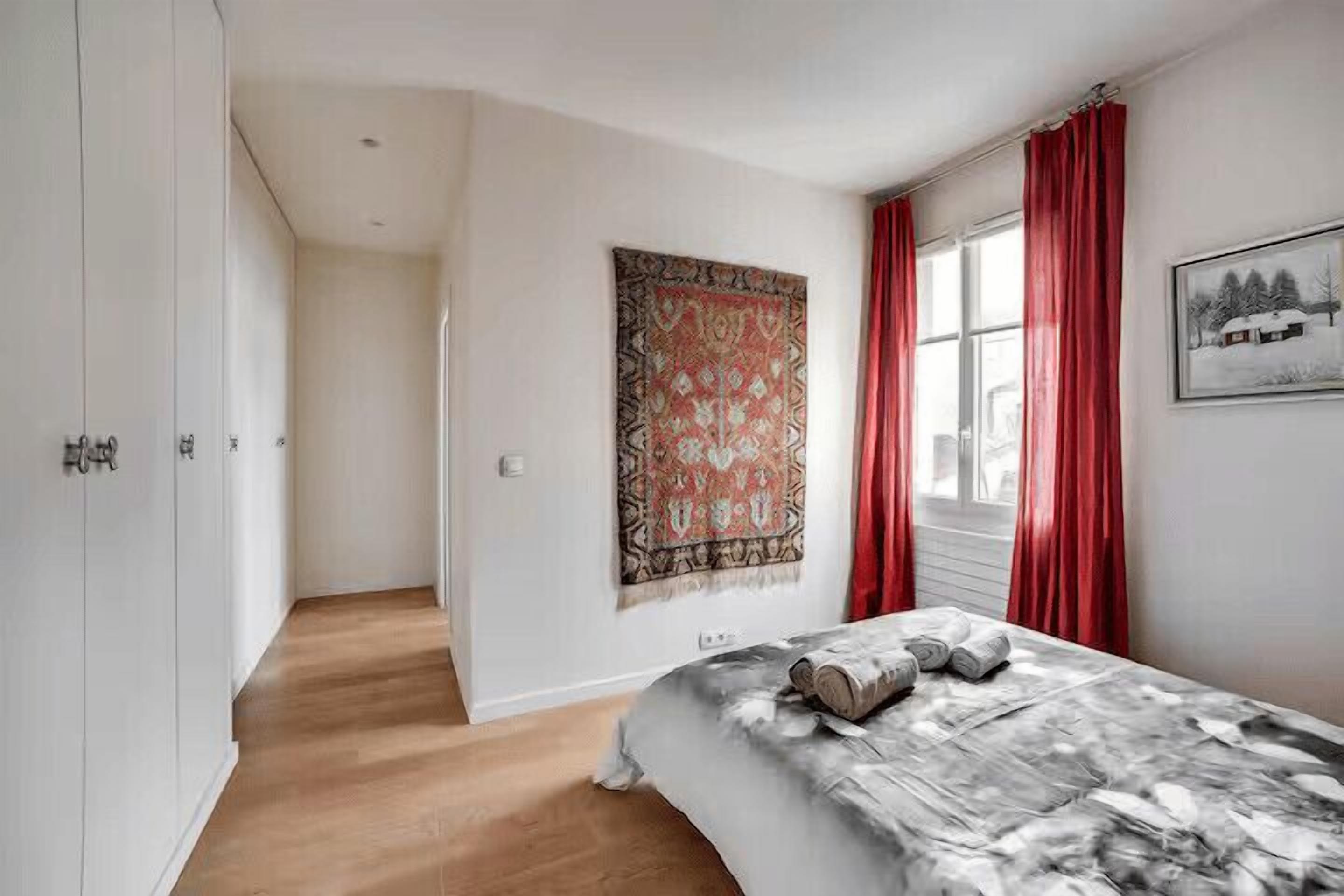 Ein Schlafzimmer mit Bett, einem Fenster mit roten Vorhängen, einer Wandweberei und einem Flur.