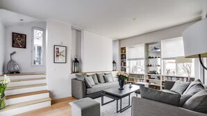 Un salon moderne avec un canapé gris, une table basse, une bibliothèque et un escalier.