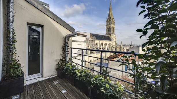 Un balcon agrémenté de plantes, une porte et une vue sur le clocher d’une église historique.