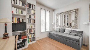 Un salon moderne avec un canapé gris, une grande bibliothèque, un miroir décoratif et une lampe.
