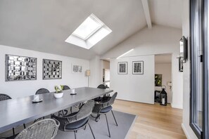 A modern dining area with a long table, wicker chairs, and framed artwork on the walls. - 100 m² terrace, parking, view of the Eiffel Tower (Saint-Cloud)