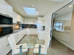 A modern kitchen with white cabinetry, a glass dining table, and a view through the glass door. - Rooftop sea view with private pool (La Rochelle)