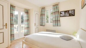 A bedroom with a bed, curtains, a wall-mounted picture, and a door leading to an outdoor area. - Villa with heated pool in Sainte-Maxime (Sainte-Maxime)