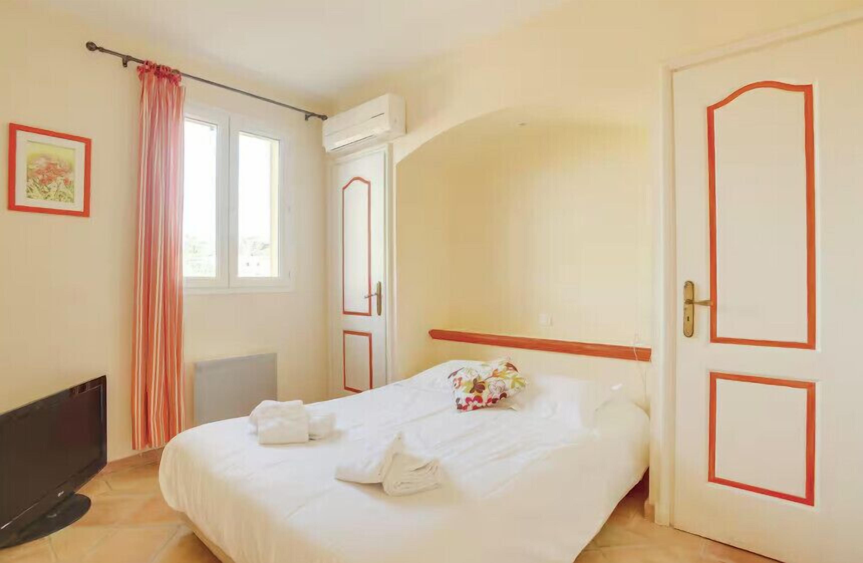 Ein Hotelzimmer mit einem Bett, einem Fernseher, einem Fenster mit Vorhängen und einer Tür mit rotem Rahmen.