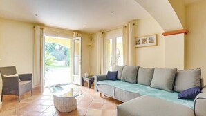 A living room with a sofa, armchair, and coffee table, a door leading outside, and a framed picture on the wall. - Villa with heated pool in Sainte-Maxime (Sainte-Maxime)