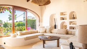 Ein modernes Wohnzimmer mit einer gebogenen Couch, einem runden Couchtisch und einem großen Fenster mit Blick auf Grünflächen.