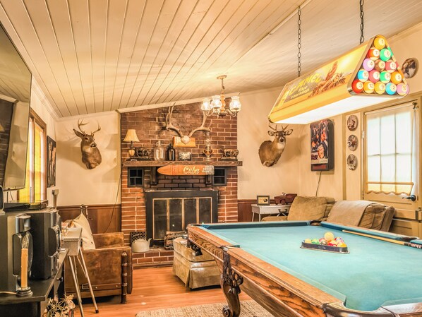 A cozy room with a pool table, a brick fireplace, and mounted deer heads.