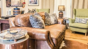Ein Wohnzimmer mit braunem Ledersofa, einem grünen Sessel, einem Couchtisch aus Holz und einem gerahmten Bild an der Wand.