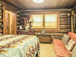 A log cabin room with a bed, a sofa, a lamp, a fan, and a window with curtains.
