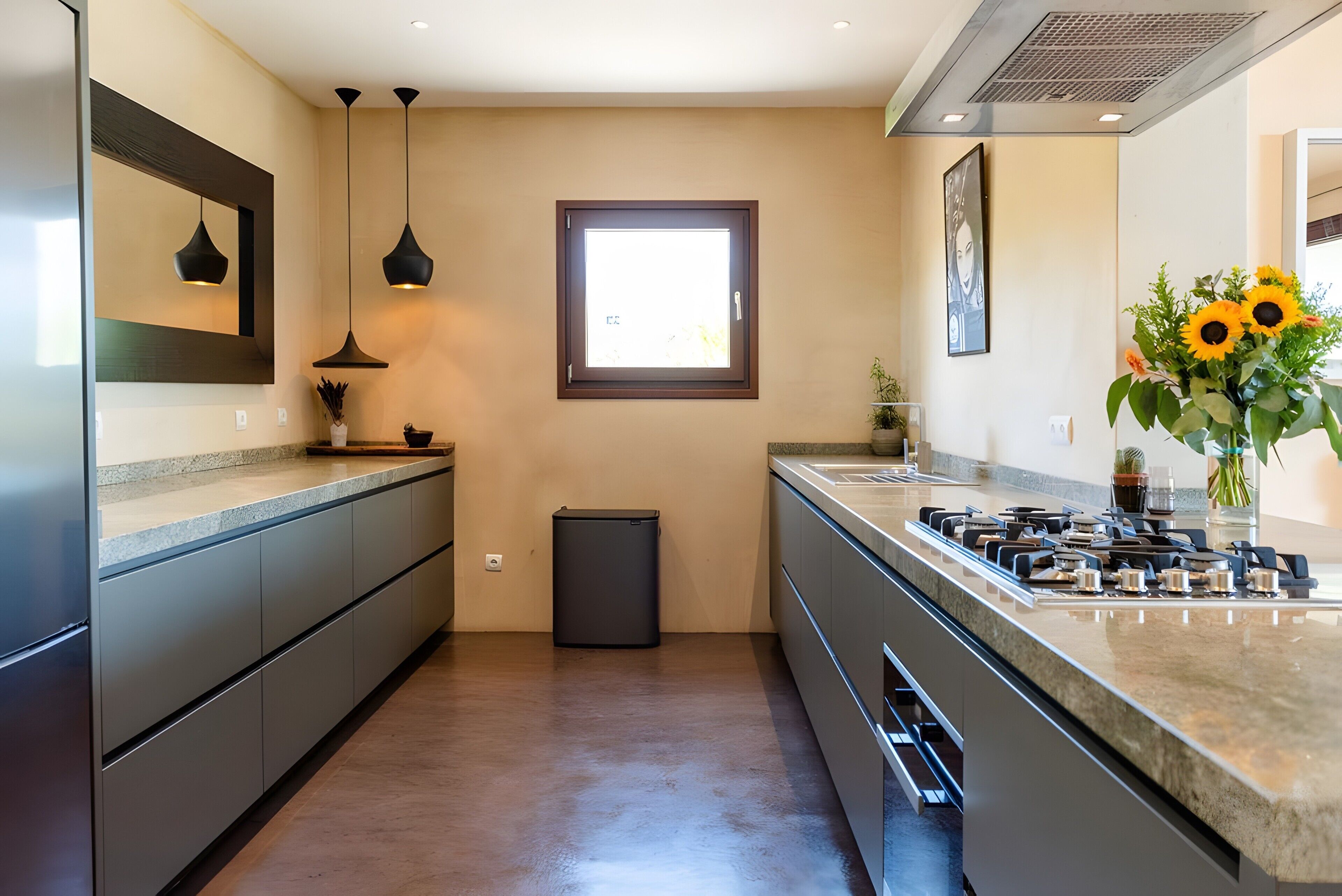 Una cocina moderna con horno empotrado, electrodomésticos de acero inoxidable, iluminación colgante y ventana con vistas.