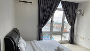 Een hotelkamer met een bed, een raam met gordijnen, uitzicht op een zwembad en een ventilator aan de muur.