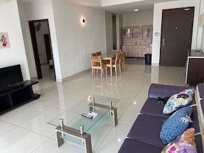 A modern living room with a glass coffee table, a sofa with patterned cushions, a TV, and a dining area with chairs and a table. - KSL 2BR #10 (Johor Bahru)