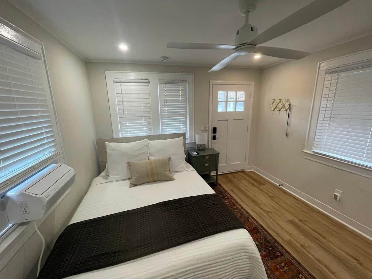 Un dormitorio con cama, mesita de noche, calentador, persianas y ventilador de techo.