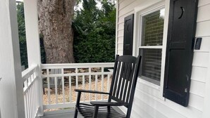 A porch with a rocking chair, white railings, and a tree in the background.