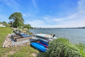 Une terrasse au bord du lac, avec des chaises longues, des kayaks et une planche à pagaie.