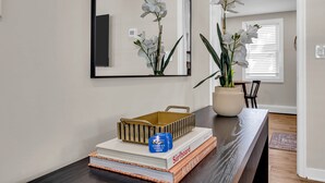 Een modern interieur met een donker houten tafel, een spiegel, witte orchideeën, een boek getiteld 'Surfboard' en een klein blauw bordje.