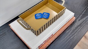 Een gesloten koffer met een handgreep, geplaatst op een oppervlak met een boek getiteld 'Surfboard' en twee blauwe kaarten met tekst.