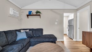Een moderne woonkamer met een hoekbank, een ronde salontafel, een houten kast en een ingebouwde airconditioning.