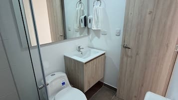Un bagno moderno con box doccia in vetro, un water bianco, un mobile bagno in legno con lavandino e uno specchio sopra lo specchio.