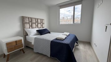 Un dormitorio con cama, mesita de noche, ventana y vista a la ciudad, además de una puerta.