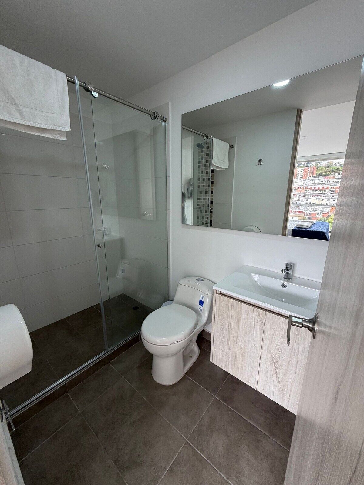 Un bagno moderno con cabina doccia in vetro, un water, un lavabo e uno specchio.
